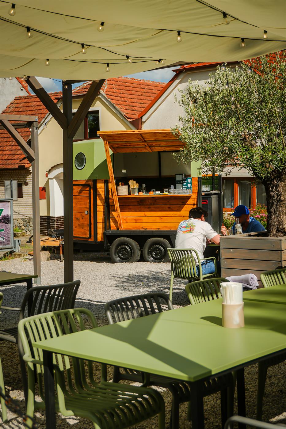 Zelené stoly na zahradě, bar a vozítko pod olivovníkem